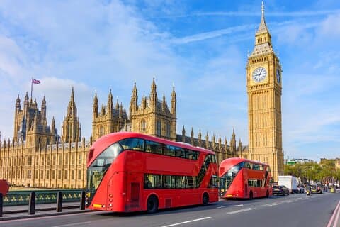 Red double-decker buses pass by the Houses of Parliament and Big Ben on Westminster Bridge, an iconic scene of London’s rich heritage.