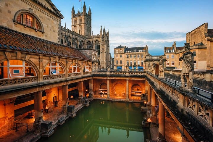 The ancient Roman Baths in Bath, with Bath Abbey towering in the background, create a perfect blend of historical architecture at dusk.