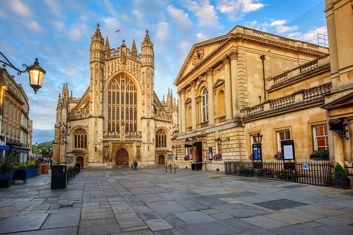 Bath Abbey stands majestically in the heart of the city, its gothic architecture illuminated against a beautiful evening sky.