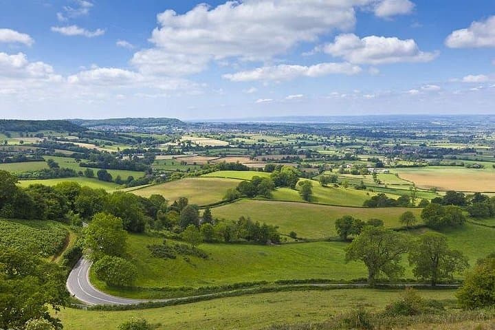 Glimpse the gentle beauty of the Cotswolds’ rolling hills, where green fields stretch across a timeless English countryside