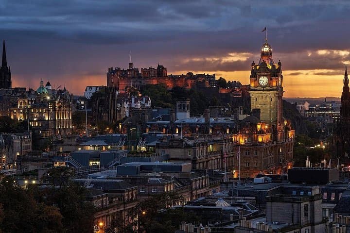 Edinburgh skyline at dusk, featuring the illuminated Balmoral Hotel clock tower and historic Edinburgh Castle against a dramatic sunset sky.