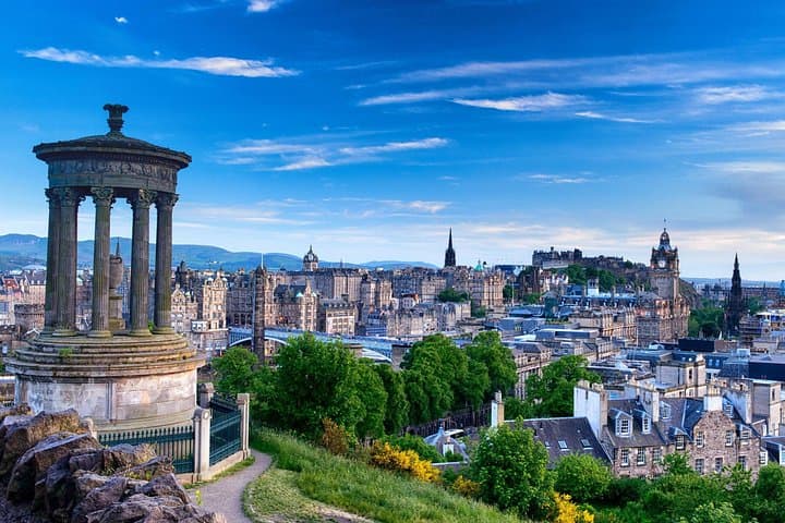 Panoramic view of Edinburgh from Calton Hill, featuring the Dugald Stewart Monument in the foreground and the historic cityscape under a clear blue sky.